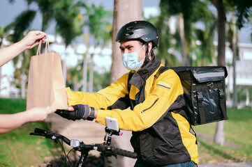 Naklejka premium Courier wearing a yellow company shirt, riding a bicycle, delivering food paper bags to customers