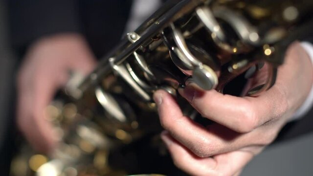 Saxophonist plays with fingers on the saxophone valves close-up. Musician in a suit presses the saxophone keys.