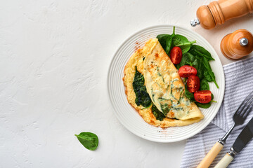 Omelet or omelette with spinach, cherry tomato and pepper seasoning on a white plate, on white background. Top view.
