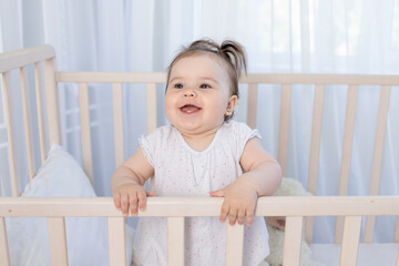 happy laughing baby girl in the crib in the nursery in a white bodysuit