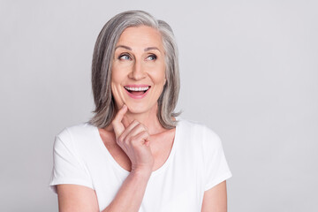 Photo of confident impressed mature lady wear white clothes finger chin looking empty space smiling isolated grey color background