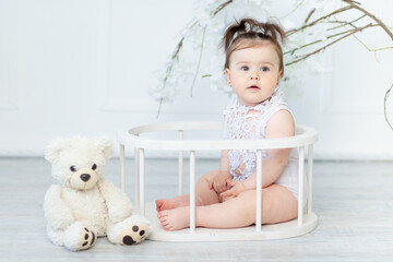 beautiful baby girl in a white bodysuit on a light background with a teddy bear