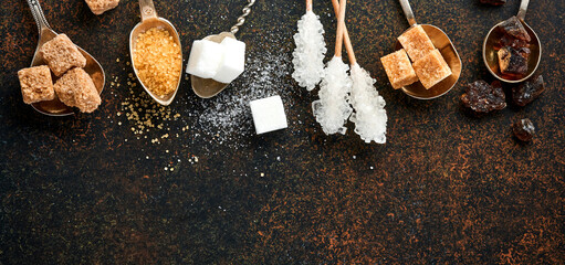 White sugar, cane sugar cubes, caramel in teaspoons on dark brown table concrete background. Assorted different types of sugar. Top view or flat lay.