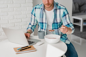 man in shirt sitting in kitchen at home at table working online on laptop