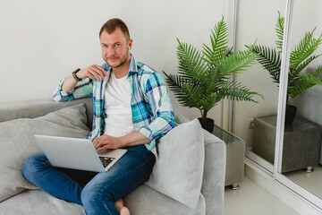 handsome busy focused man in shirt sitting relaxed on sofa at home at table working online