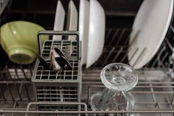 Dishwasher basket with clean dishes, glasses and cutlery in kitchen