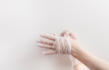 Two female hands taking off disposable vinyl gloves above neutral background. Infection prevention...