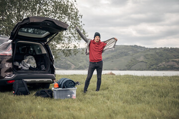 Camper packing and unpacking from a car's back door in nature.