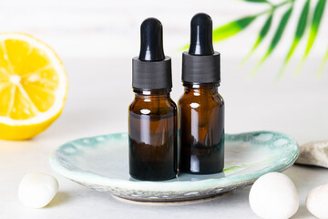 Skin care serums in glass bottles with dropper on light background with lemon and palm leaves. Skin care in summer time concept. SPF and beach cosmetic. Vitamin C cosmetic products.