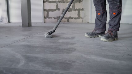 Worker cleans seams between tiles using a vacuum cleaner. Tile master, vacuums the floor to prepare...