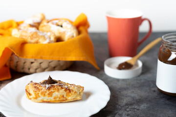 Chocolate-filled puff pastry Neapolitan with basket of puff pastry sweets, coffee cup, open jar of chocolate and spoon with chocolate spread. Selective focus