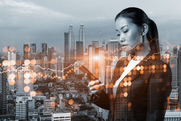 Attractive Asian businesswoman trader checking quotes to forecast the capital market behavior. Concept of trading strategy. Forex chart. Kuala Lumpur. Double exposure.