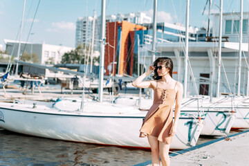 young beautiful healthy woman walks along the pier against the background of the yacht pier. Sea port in summer. A weekend trip.