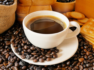 A hot coffee in a white cup and 
crackers and breads and more coffee beans on the table and in the sack