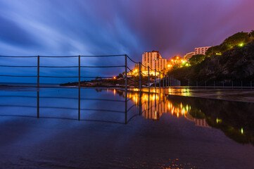 Reflection of railing on pier in front of coastal buildings
