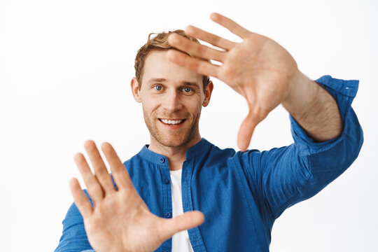 Just imagine. Smiling redhead man picturing something, looking through hand frames gesture and dreaming, explain his vision, feeling creative, standing over white background