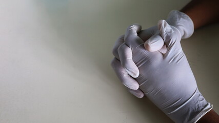 Wear interlocking white latex surgical gloves. Man's hand wearing anti-disease gloves on a gray-white table background in a dark, slightly lit room with copy space. Close up