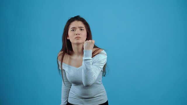 The angry young woman points her finger at her nose, you are not ashamed, then she points with her fist, you will be beaten. Asian with dark hair, dressed in a blue blouse, isolated on a dark blue
