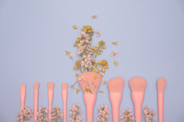 Set of pastel pink professional make up brush set and flowers on pastel blue background. top view...