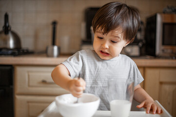 Obraz na płótnie Canvas a little boy eats breakfast, eats porridge and drinks milk