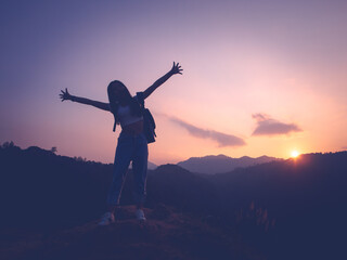 Silhouette of woman enjoying the sunset with dramatic sky on mountain peak.