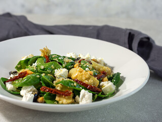 Summer salad of spinach leaves, olives, sun-dried tomato, feta cheese and soy asparagus on a white plate and light background with a dark napkin. Summer menu concept. horizontal arrangement. Close-up.