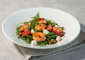 Fresh summer salad with shrimps, strawberries, olives, mozzarella and rucola in a white plate on a light background. Summer menu concept. Close-up