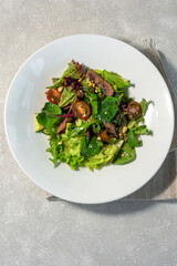 Summer salad of spinach leaves,sun-dried tomato, olives, feta cheese and soy asparagus on a white plate and light background. Summer menu concept.
