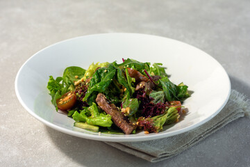 Summer salad with meat and lettuce, arugula and spinach, cherry tomatoes and cucumber on a white plate on a light background. Summer menu concept. horizontal arrangement.