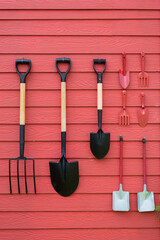 Metal gardening tools put to slot made from wood On the red wall . Gardening tools concept.