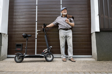 A positive, elderly man stands near the door and holds an eco scooter behind the wheel. Healthy lifestyle of the elderly.