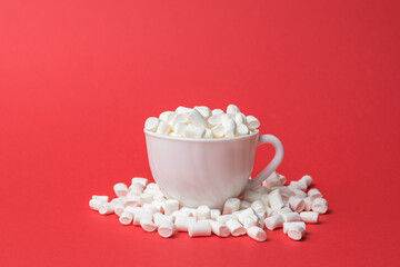 Fototapeta na wymiar A white mug filled with marshmallows on a red background.