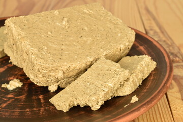 Several slices of vanilla halva on a clay plate, close-up, on a wooden table.