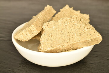 Several slices of vanilla halva in a white ceramic bowl, on a slate board, close-up.