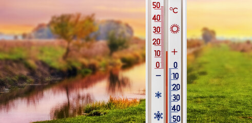 The thermometer shows plus 15 degrees on the background of the river during sunset in autumn. Fall...