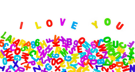Multicolored letters from alphabet are lined with words I love you on white background as wave. Colorful plastic English letters from children's designer are scattered randomly. Declaration of love
