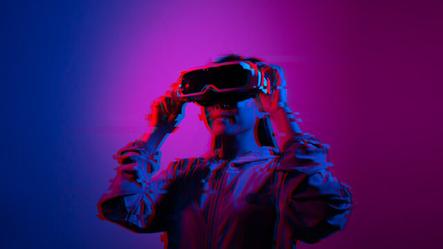 Glitch Effect of Young woman using glasses of virtual reality. Smartphone using with VR headset,virtual reality,future technology concept.Asian woman using VR glasses in colorful neon lights.