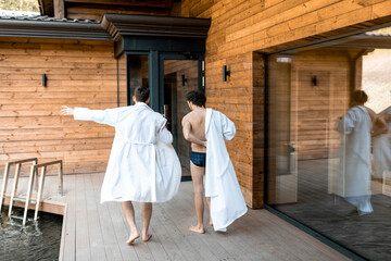 Fototapeta na wymiar Company of male friends walking on the terrace in spa complex while dressing on the go their bathrobe. Relax and fun time in wellness spa. 
