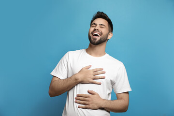 Young man laughing on light blue background. Funny joke