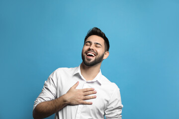 Young man laughing on light blue background. Funny joke