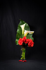 Beautiful bouquet of flowers and leaves of arum and red roses, on a black background