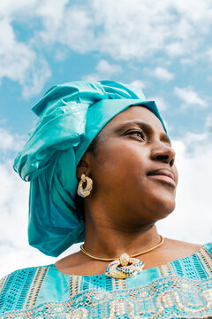 West African woman with headwrap smiling with sky in background