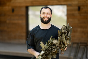 A portrait of the bathhouse attendant with oak broom for the bath. Cheerful male personal in spa.