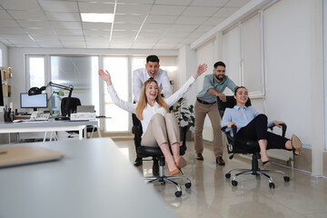 Fototapeta premium Happy office employees riding chairs at workplace