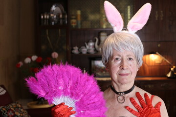 Fun senior woman with bunny ears and feathers hand fan - obrazy, fototapety, plakaty