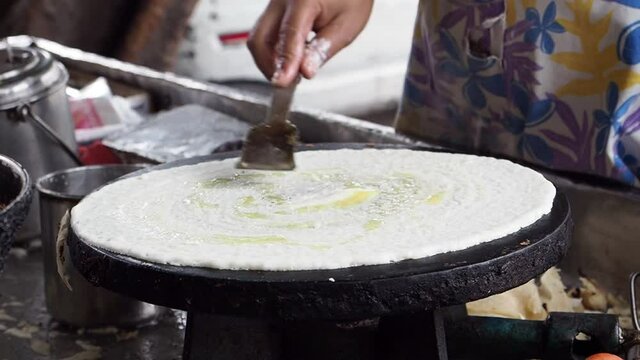 KOLKATA, INDIA - May 02, 2021: Closeup of making steaming hot 'Dosa' on a cast iron pan. Dosa is the Indian version of pancake made with rice flour dough