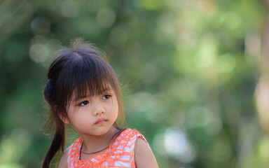 A little adorable Asian girl with sad eyes walking in the park alone.