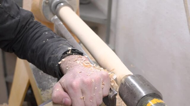 Working on a lathe.Woodworking and manufacturing of furniture made of wood and boards.Woodworking industry.A man cuts patterns on a tree and wood shavings fly.Workshop wood processing plant.