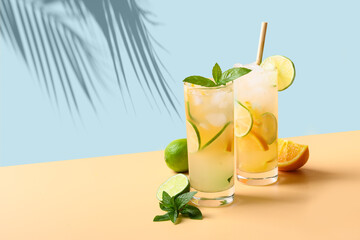 Two summer cold mojito cocktails with orange and lime slices on blue and beige background. Refreshing summer beverage with sunny shadow. - obrazy, fototapety, plakaty