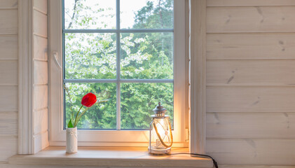 White window with mosquito net in a rustic wooden house overlooking blooming spring garden, pine forest.